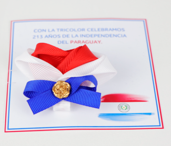 Escarapela tricolor con un dije dorado, con tarjeta tematica de festividades patrias